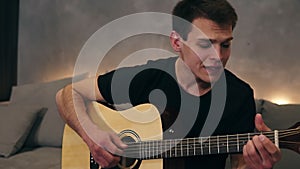 Portrait of a cheerful man singing a lyric, emotional song. Playing on an acoustic guitar and enjoying it, while sitting