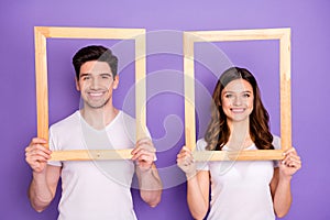 Portrait of cheerful man woman hold wooden picture frame wear white t-shirt casual style isolated over violet color