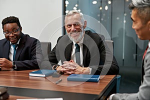 Portrait of cheerful mature businessman in formal wear looking at camera and smiling while having a meeting in the