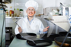 Portrait of cheerful mature man cook with frying pans on kitchen