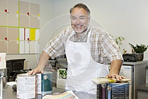 Portrait of a cheerful mature sales clerk with paint can in hardware store