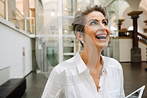 Portrait of cheerful mature woman art gallery manager holding tablet while standing in museum