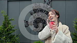 Portrait cheerful middle-aged lady talking on cellphone the street. Cup coffee