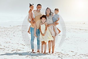 Portrait of a cheerful mixed race family with three children standing together at the beach and smiling while looking at