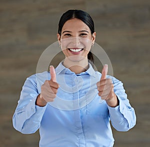 Portrait of a cheerful mixed race smiling businesswoman showing thumbs up gesture at work. Young hispanic woman showing