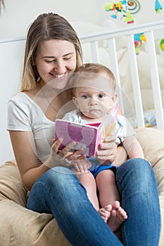 Portrait of cheerful mother reading book to her baby boy at living room