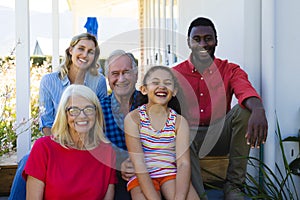 Portrait of cheerful multiracial multigeneration family sitting outside house in yard