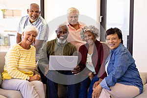 Portrait of cheerful multiracial senior friends with laptop relaxing on sofa at nursing home
