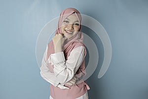 Portrait of a cheerful Muslim Asian woman standing and smiling at the camera,  on blue background
