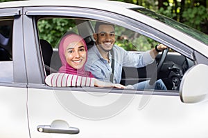 Portrait of cheerful muslim spouses sitting in car and smiling at camera