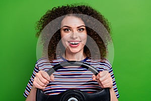 Portrait of cheerful nice girl toothy smile arms hold steering wheel isolated on green color background