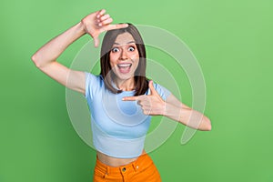 Portrait of cheerful overjoyed funky lady arms fingers demonstrate cadre gesture isolated on green color background