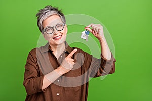 Portrait of cheerful person with white gray hairstyle in glasses directing at keys from new house isolated on green