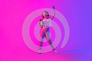 Portrait of cheerful playful little girl singing on pink futuristic background