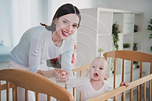 Portrait of cheerful positive girl hold hand cute toddler wooden bed crib free time weekend indoors