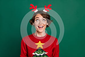 Portrait of cheerful positive lady toothy smile look up deer antlers accessory isolated on green color background