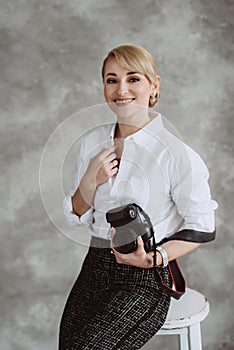 Portrait of a cheerful positive optimistic young woman photographer in the studio with a camera, on a gray background. Soft