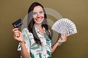 Portrait of cheerful pretty girl toothy smile hands hold dollar bills debit plastic card  on brown color