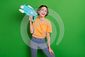 Portrait of cheerful pretty lady arm hold water gun toothy smile laughing isolated on green color background