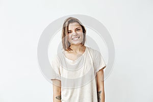 Portrait of cheerful pretty tattooed girl smiling biting lip looking at camera over white background.