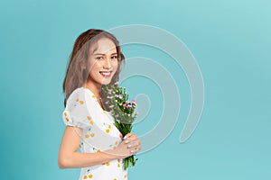Portrait of a cheerful pretty woman holding flowers over blue background