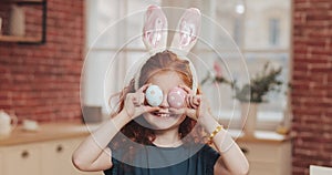 Portrait of cheerful redhead little kid girl with bunny ears with an easter egg on the kitchen background. She is