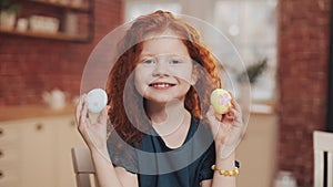 Portrait of cheerful redhead little kid girl playing with easter egg on the kitchen background. She is cheering and