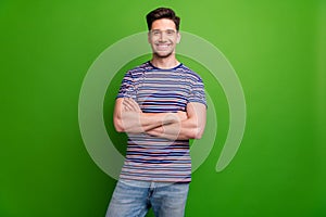 Portrait of cheerful satisfied young man beaming smile crossed hands posing isolated on green color background