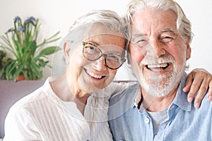 Portrait of cheerful senior couple embracing and laughing. Elderly happy couple relaxing in front of camera sitting in living room