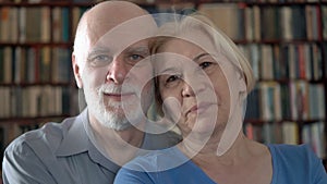 Portrait of cheerful senior couple at home. Having good time. Bookcase bookshelves in background