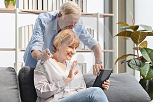 Portrait of Cheerful senior couple in living room, Mature woman and senior man using smartphone talking on video call on cozy sofa