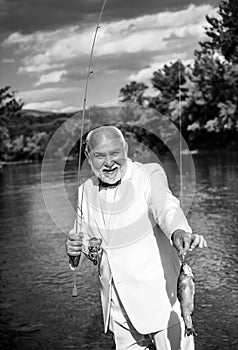 Portrait of cheerful senior man fishing. Grandfather with catch fish. Mature man fisherman in white suit and bowtie with