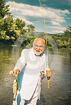 Portrait of cheerful senior man fishing. Grandfather with catch fish. Mature man fisherman in white suit and bowtie with