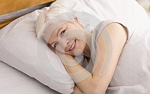 Portrait of cheerful senior woman resting in bed