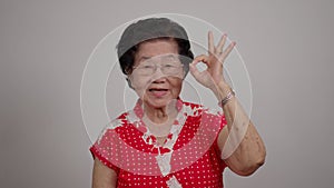 Portrait cheerful smiling Asian senior woman wear glasses grey hair over isolated white background locking the camera and show ok