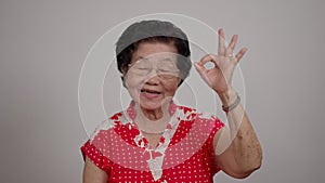 Portrait cheerful smiling Asian senior woman wear glasses grey hair over isolated white background locking the camera and show ok