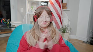 Portrait of cheerful smiling Asian teenage girl waving at camera and talking. Joyful teen blogger in headphones sitting