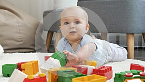 Portrait of cheerful smiling baby boy playing with colorful bricks and blocks on floor at living room. Concept of