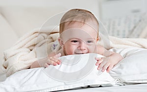 Portrait of cheerful smiling baby boy relaxing on white pillow o