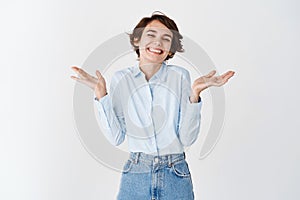 Portrait of cheerful smiling woman, shrugging and laughing flattered, being praised, receive compliments on white