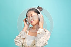 Portrait of a cheerful stylish young woman standing isolated over blue background, listening to music with headphones, dancing