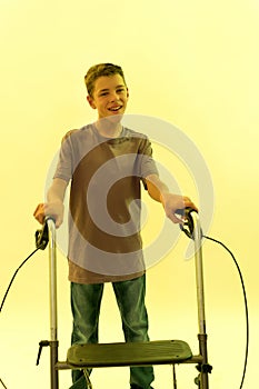 Portrait of cheerful teenaged disabled boy with cerebral palsy smiling at camera, taking steps with his walker isolated