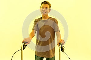 Portrait of cheerful teenaged disabled boy with cerebral palsy smiling at camera, taking steps with his walker isolated