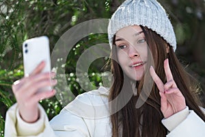 Portrait cheerful teenager girl using smartphone, showing gesturing peace sign, sending video selfie