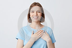 Portrait of cheerful tender young woman wears blue t shirt put hands on her heart area and feels love isolated over white