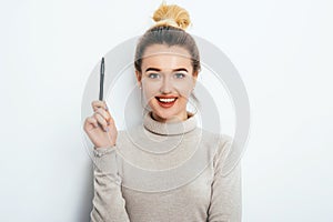 Portrait of cheerful woman with appealing smile, having hair bun in sweater isolated on white background holding pen and have a gr