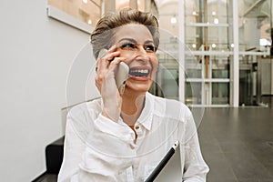 Portrait of cheerful woman art gallery manager talking on cellphone while standing in museum