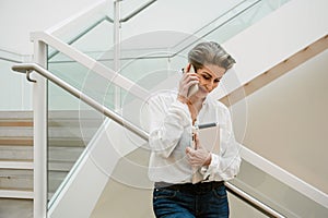 Portrait of cheerful woman art gallery manager talking on cellphone while standing in museum