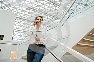 Portrait of cheerful woman art gallery manager talking on cellphone while standing in museum