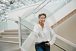 Portrait of cheerful woman art gallery manager talking on cellphone while standing in museum